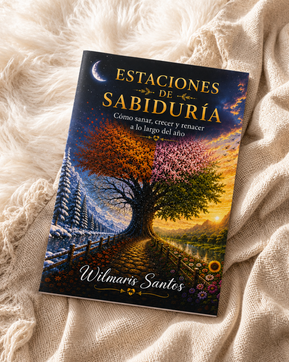 The book 'Estaciones de Sabiduría' by Wilmaris Santos is displayed on a soft, beige knitted blanket. The cover features a highly detailed, colorful illustration of a tree with autumn and spring foliage, set against a sunset sky with a crescent moon.
