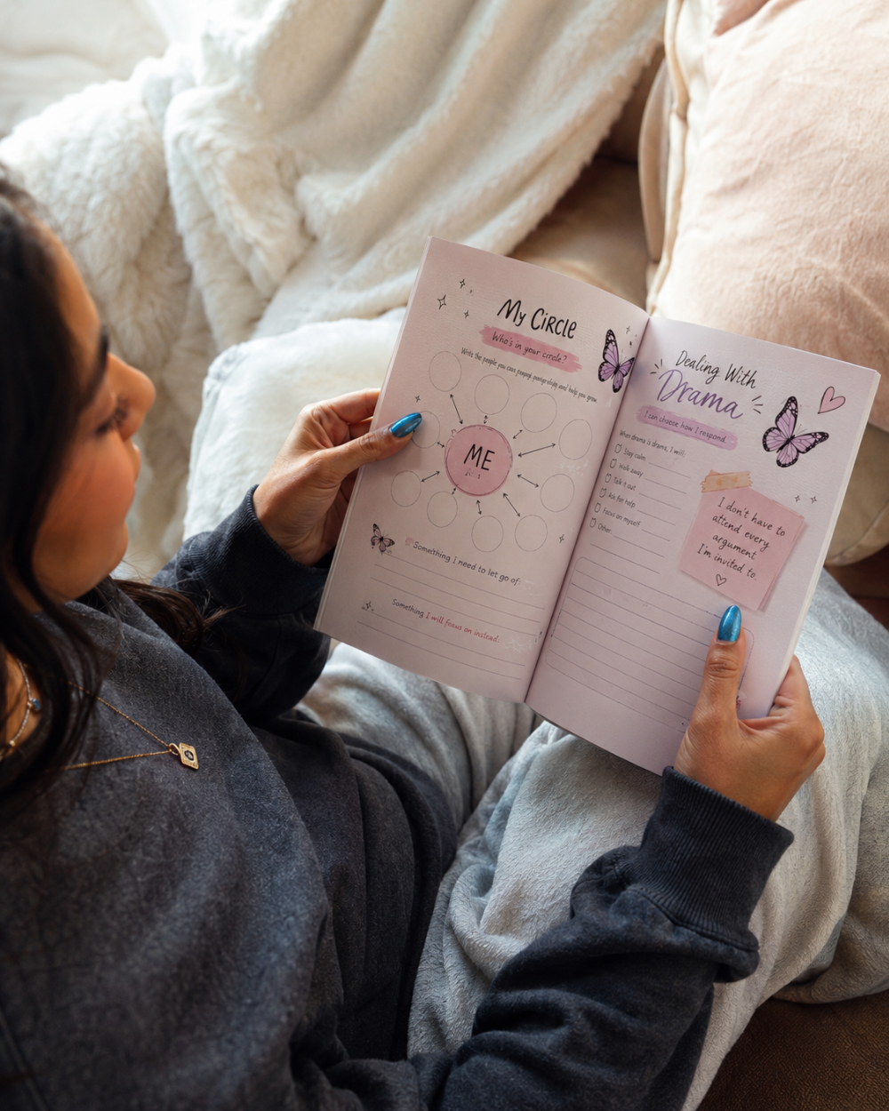 A person sitting on a couch holding an open journal. The pages are white with pink and black text and illustrations, including the title 'My Circle' and 'Feeling With Drama'.