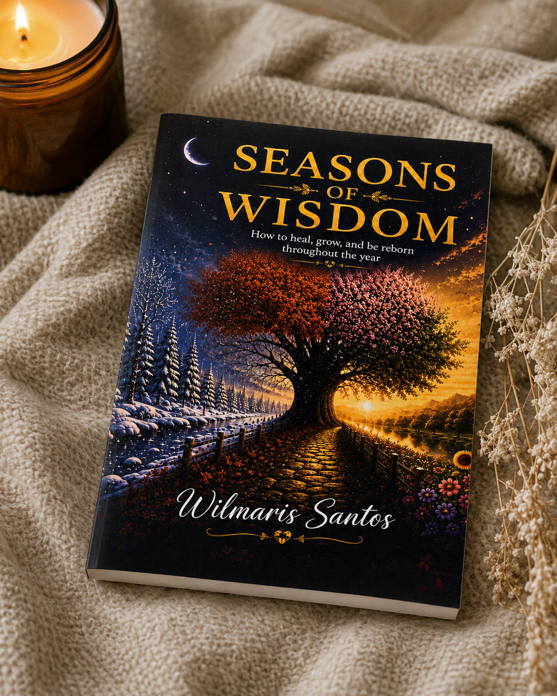 A hardcover book titled 'Seasons of Wisdom' by Wilmaris Santos, featuring a cover illustration of a tree with autumn and winter scenes, styled on a beige knit blanket next to a lit candle and dried flowers.