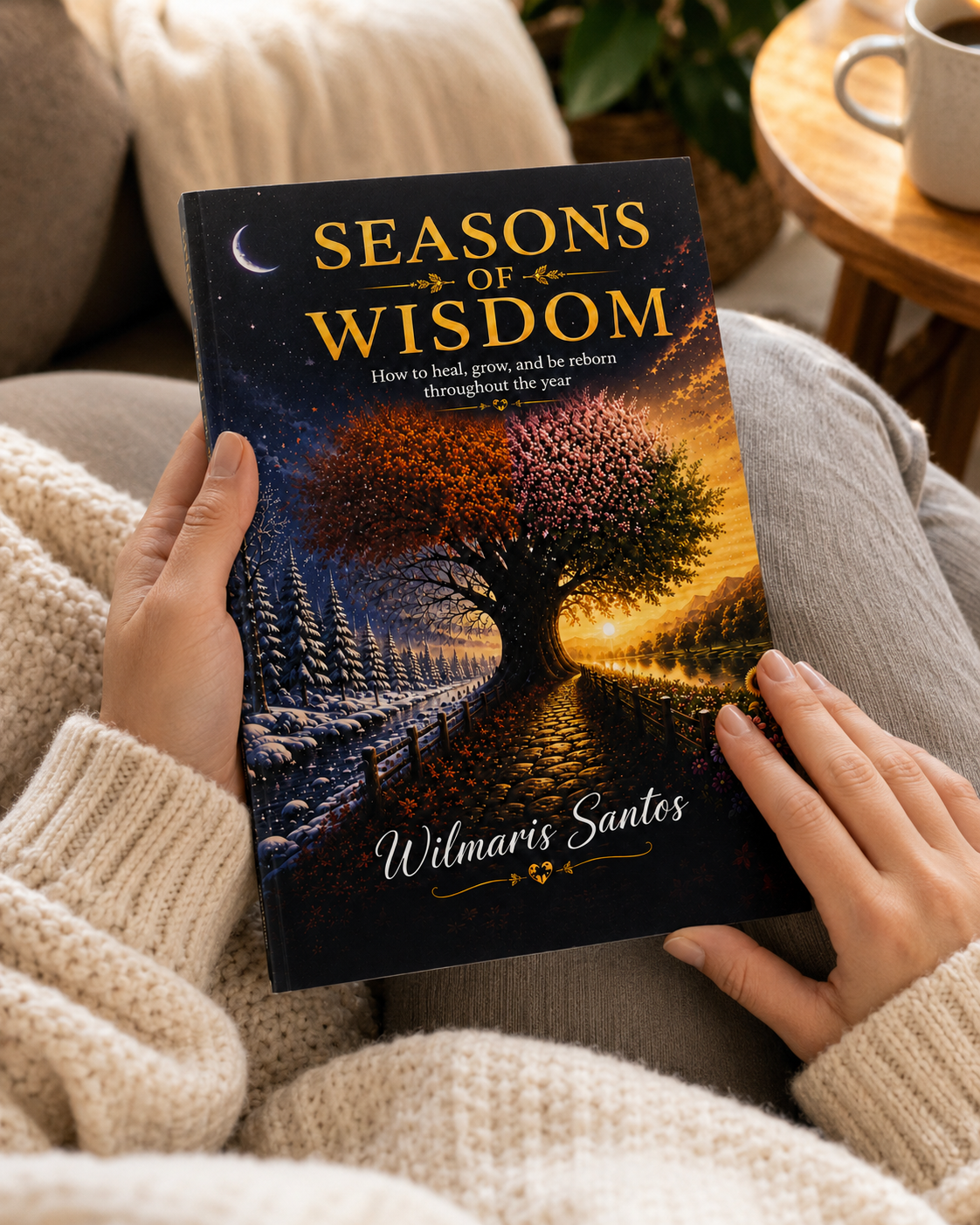 A person holding a hardcover book titled "Seasons of Wisdom" by Wilmaris Santos. The book cover features a tree with autumn and winter halves, set against a cozy indoor background with a person wearing a cream knit sweater.