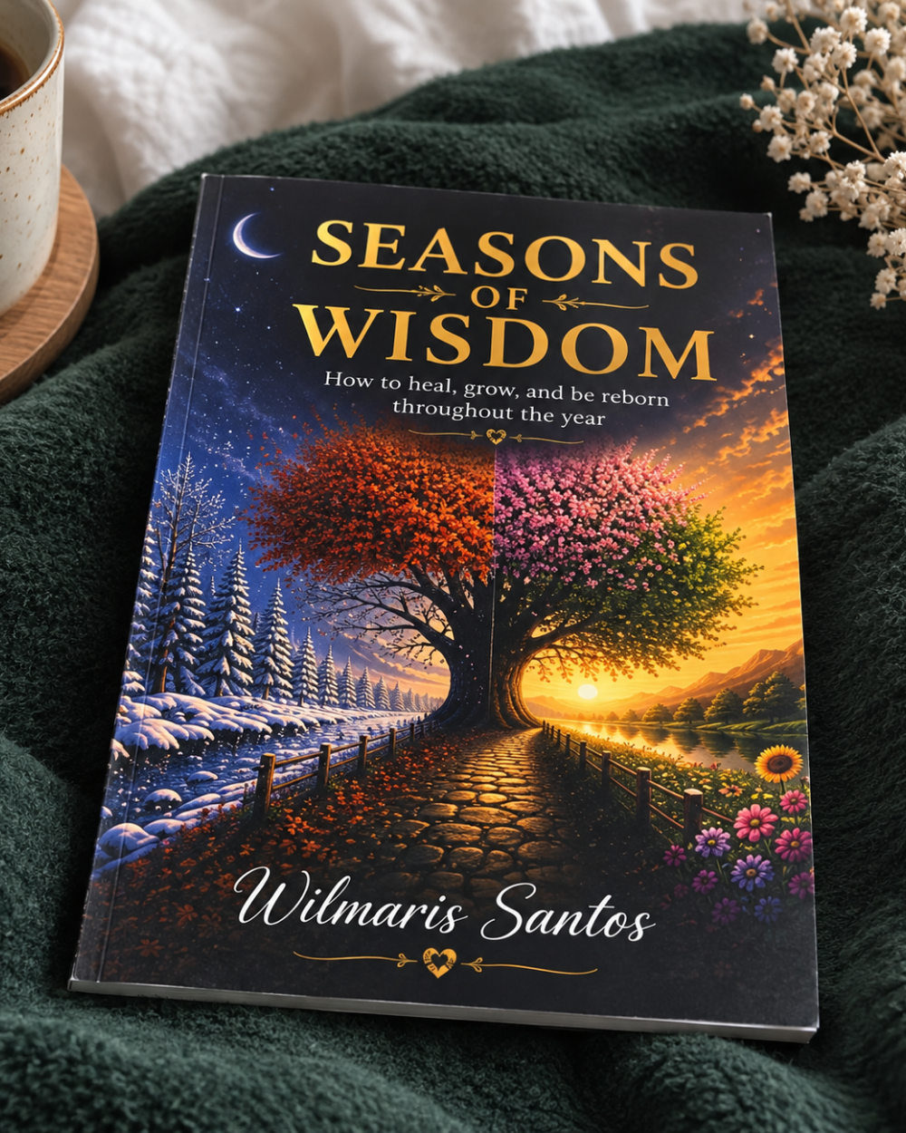 The book 'Seasons of Wisdom' by Wilmaris Santos is displayed on a dark green textured blanket next to a coffee cup and dried flowers. The cover features a beautiful illustration of a tree with autumn and spring foliage, with the title in gold lettering.