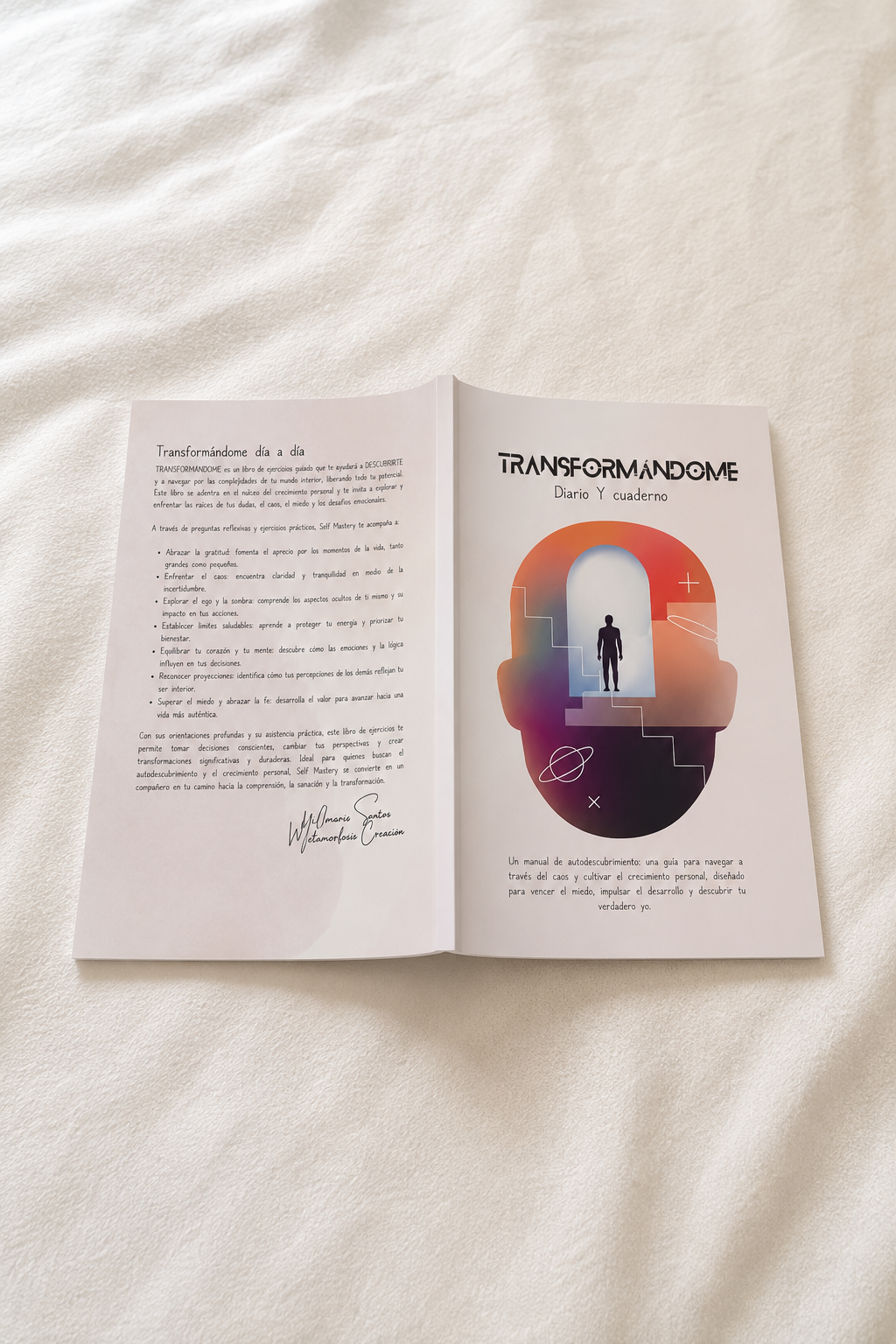 An open book laid flat on a white fabric surface. The pages contain printed text and a central graphic showing a stylized human head silhouette with a figure inside and the title 'Transformandome by Wilmaris Santos'.